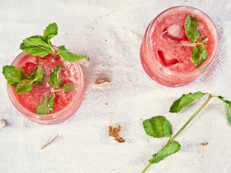  A top down shot of two red cocktails garnished with greenery on a white table cloth